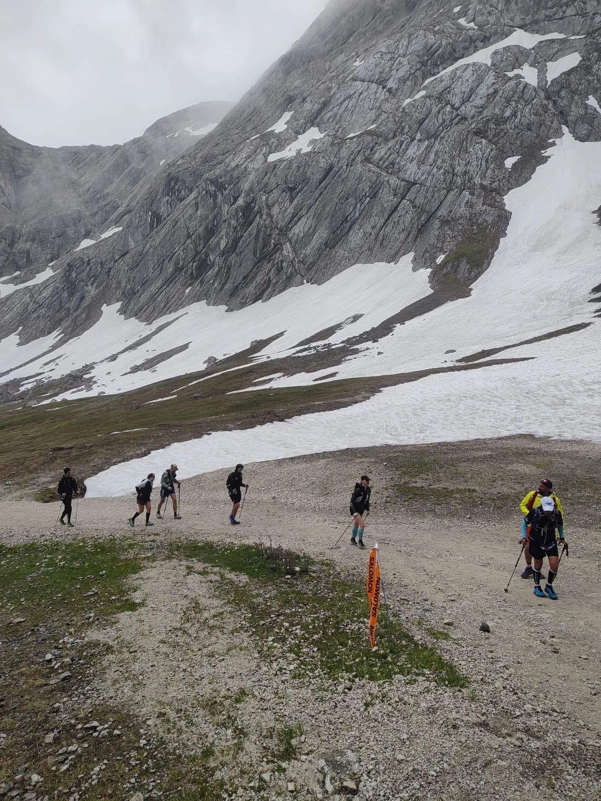 Group of ultra runners hiking past a snowfield in the Alps