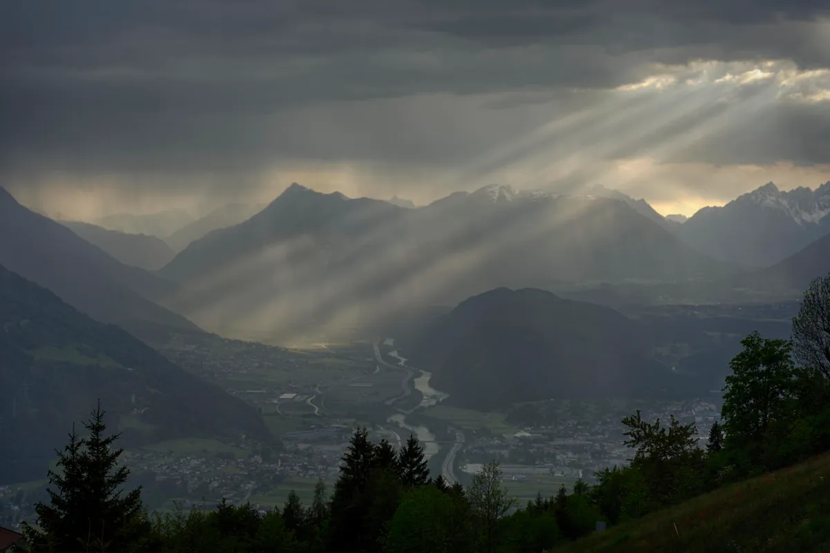 Sun rays piercing storm clouds over a deep alpine valley